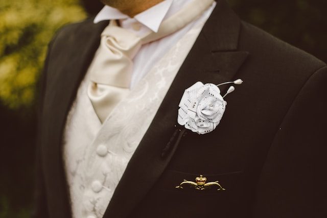 A groom in formal dress with a cream cravat, vest and a paper-rose boutonniere