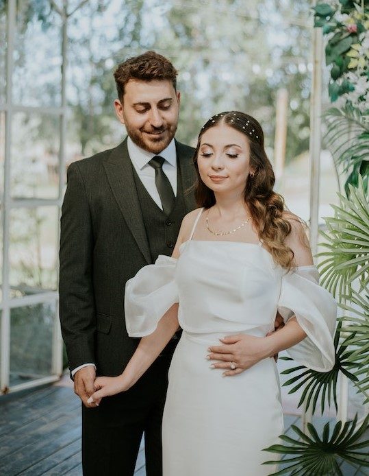 A groom in a dark three-piece suit with a bride in a white off-the-shoulder dress