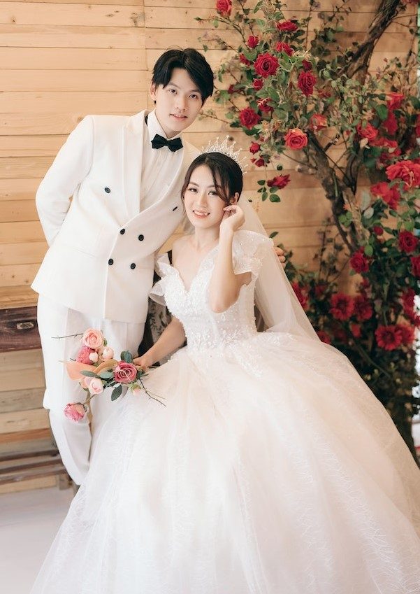 A groom in a white tuxedo and a bride in a ball gown with a rose bouquet