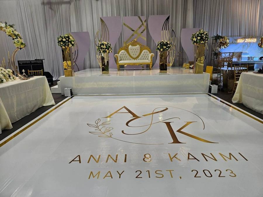 A white dance floor with a gold monogram and names decal in front of a stage with a gold loveseat