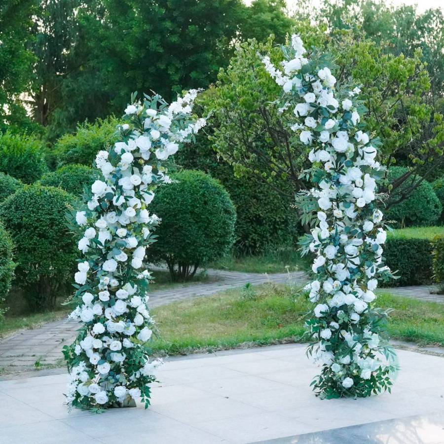 A freestanding arch of white roses and greenery on a garden terrace