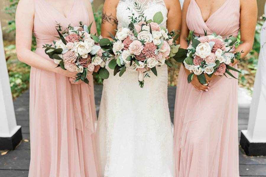 A bride and two bridesmaids in blush pink holding matching bouquets of pink and cream flowers with eucalyptus