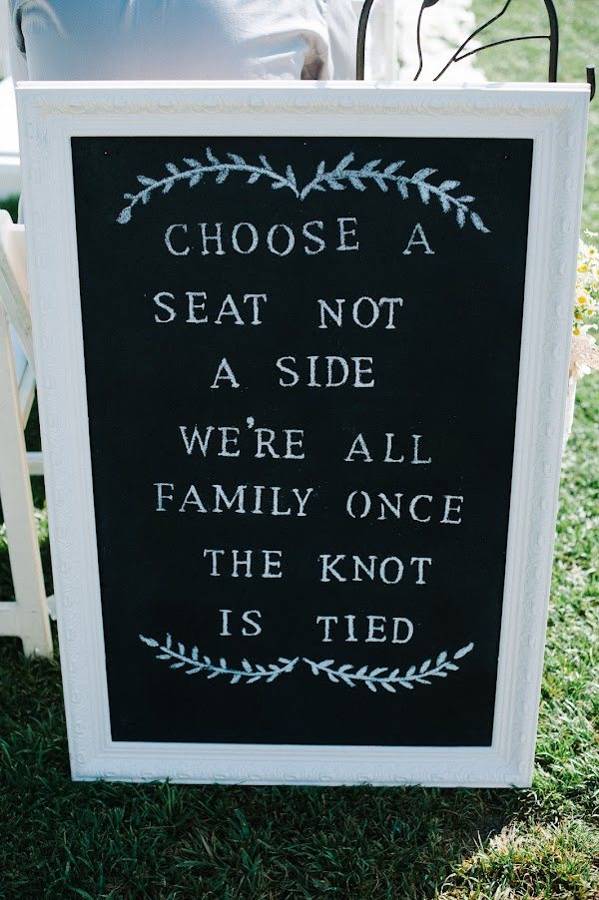 A chalkboard sign at the ceremony reading Choose a seat, not a side. We are all family once the knot is tied