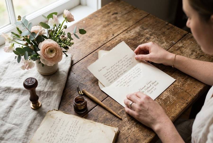 A woman folding a handwritten letter into an envelope beside pink ranunculus