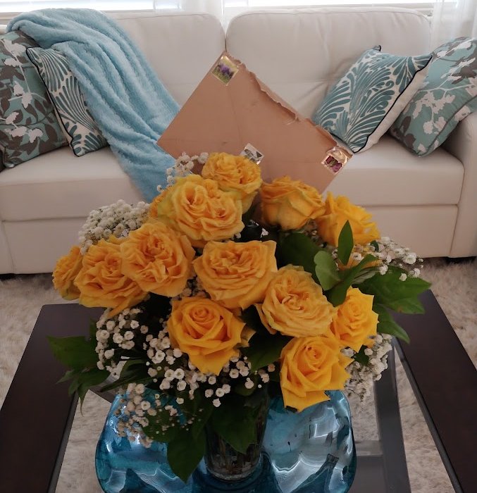 Yellow roses and baby's breath in a blue glass vase with a handwritten note tucked in behind them