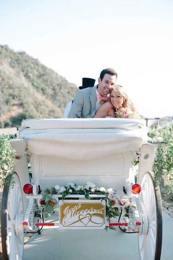 A just-married couple leaning together in the back of a decorated carriage