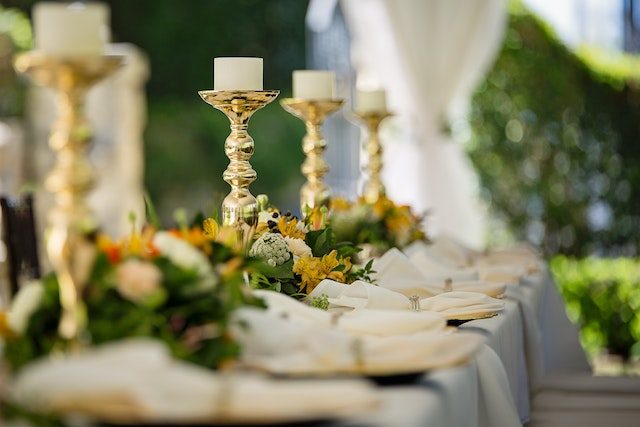 A long reception table with gold candlesticks, flowers and folded napkins