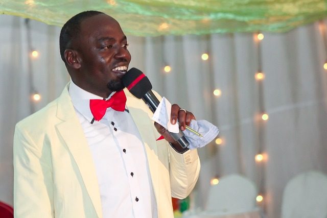 A master of ceremonies in a cream jacket and red bow tie speaking into a microphone