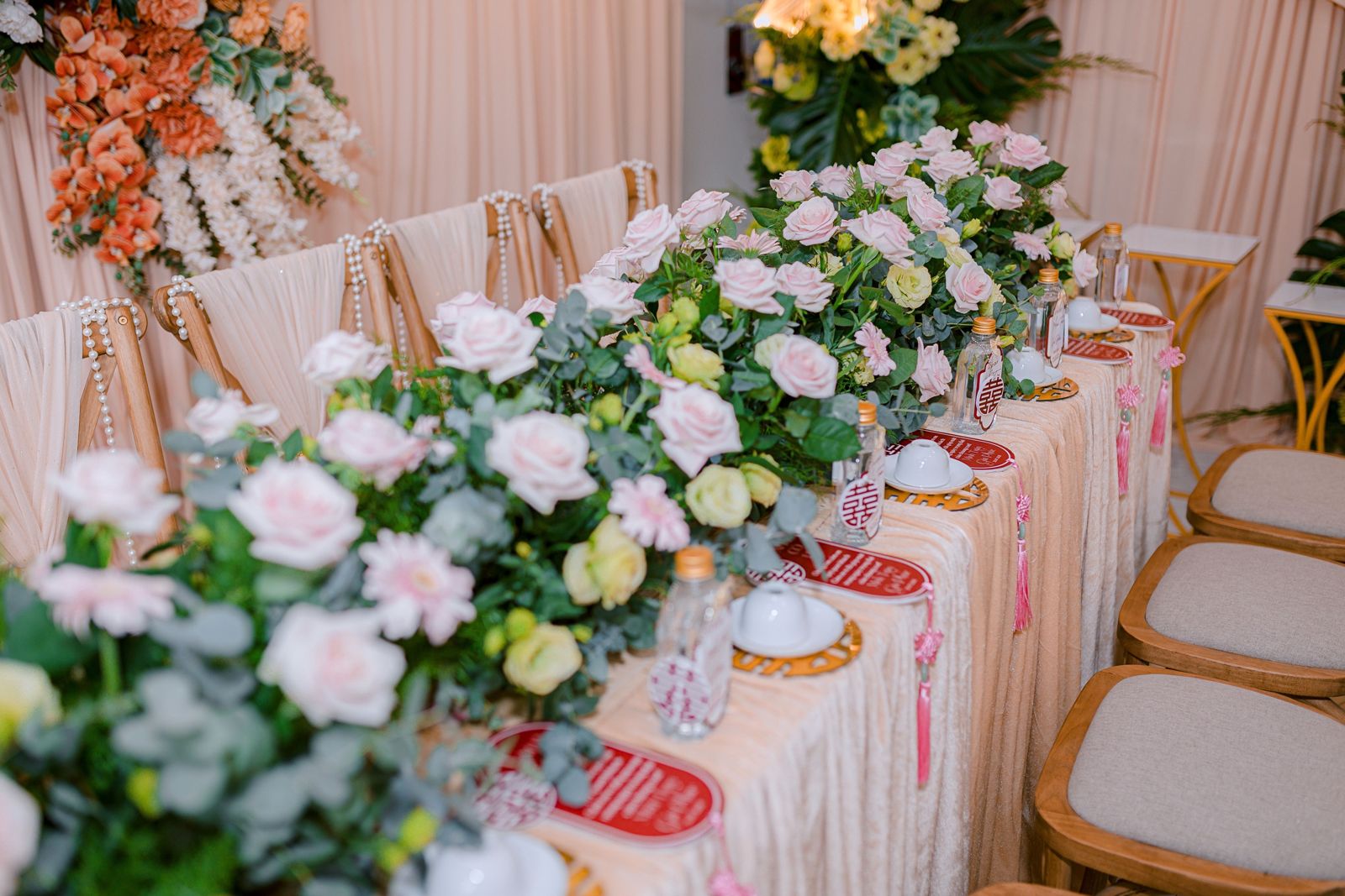 A long wedding head table lined with pink and white roses, eucalyptus and soft draped fabric