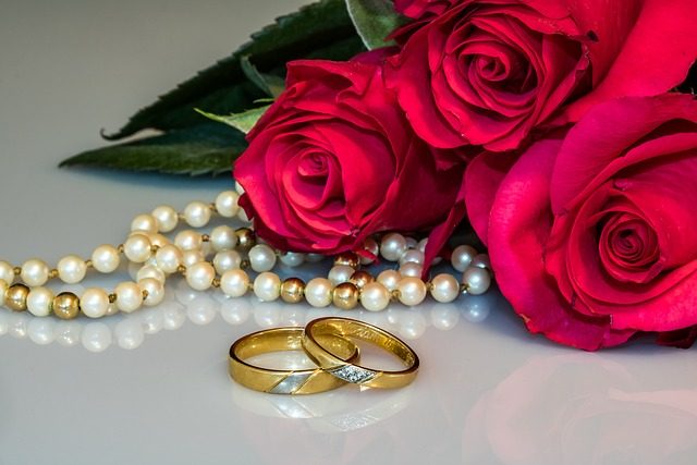 Two gold wedding bands beside a strand of pearls and red roses