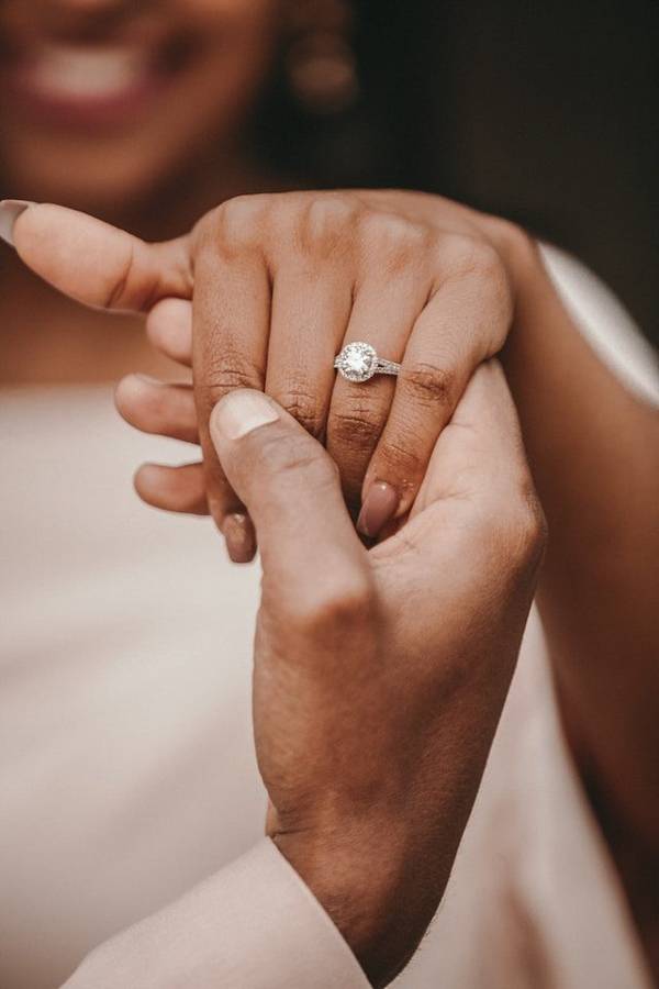 A groom holding his bride's hand to show her halo diamond engagement ring