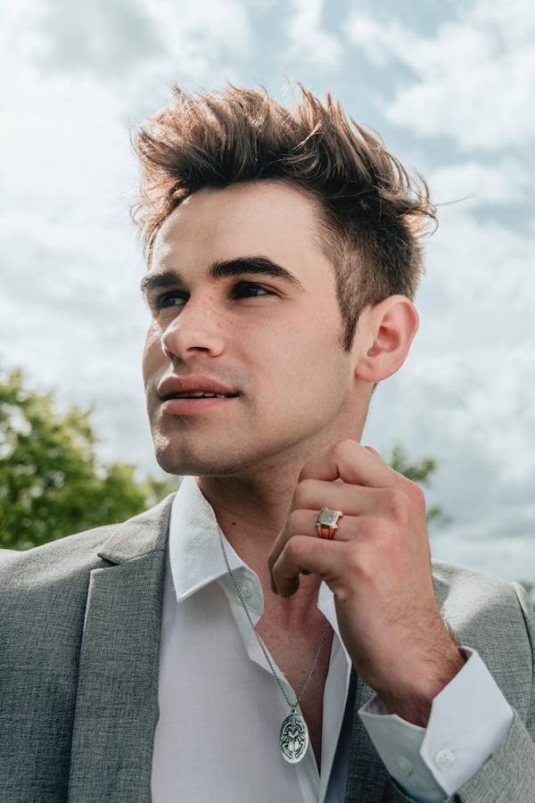 A man in a gray blazer wearing a signet ring and pendant necklace