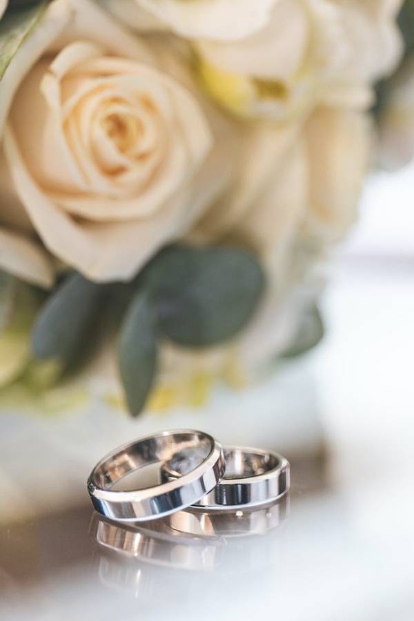 A pair of silver wedding bands in front of cream roses