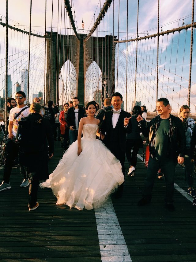 A bride and groom walking across the Brooklyn Bridge at sunset
