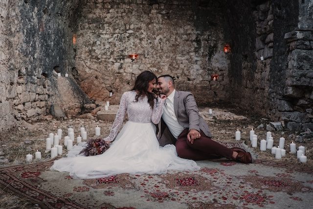 A couple seated on a rug among white candles inside old stone ruins
