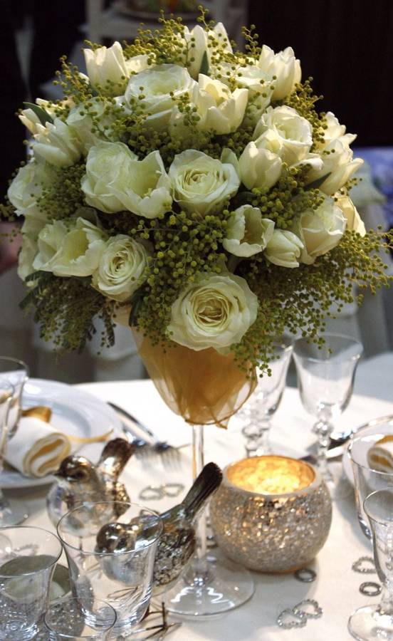 A tall centerpiece of white roses and tulips with silver birds and a glittering candle holder