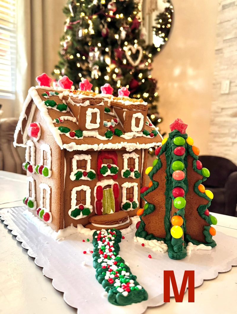 A classic gingerbread house with icing windows, candy holly, a gumdrop star roof and a candy-light gingerbread tree beside a sprinkle walkway